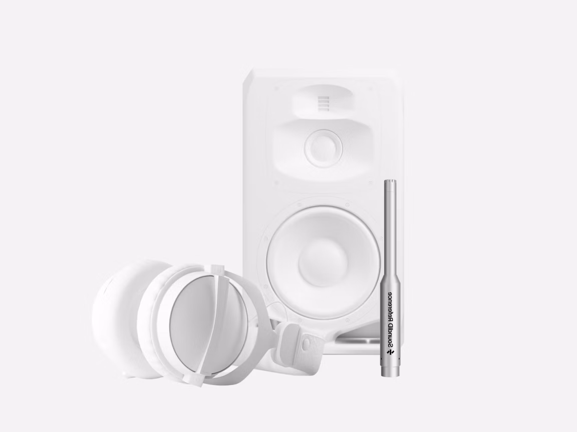White studio monitor speaker with over-ear headphones and a silver measurement microphone placed in front, minimalist front view on a light gray background for acoustic calibration setup.