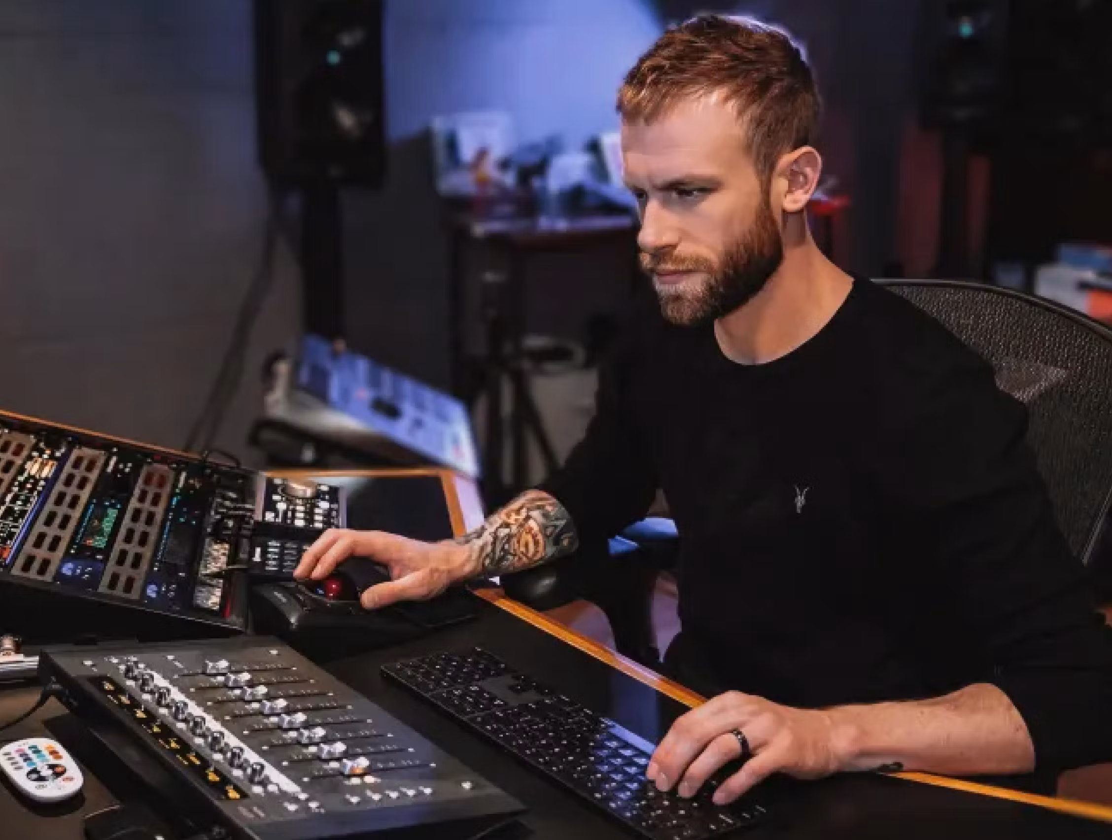 Bearded audio engineer Aaron Mattes working at a professional mixing desk with control surface and analog gear in a modern recording studio.