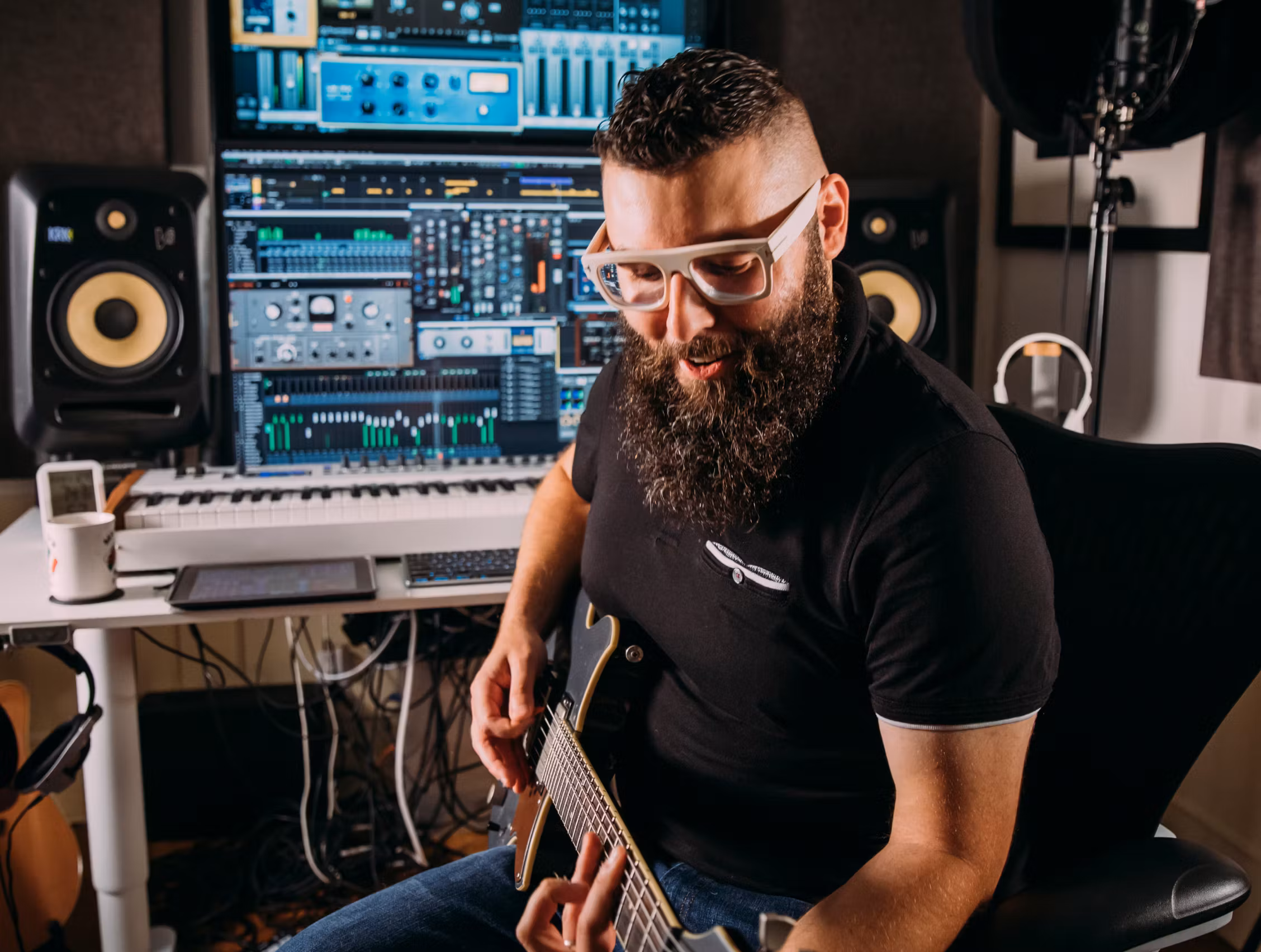 Composer, songwriter, vocalist, mixer and producer Jason Soudah with an electric guitar in a home studio; DAW on dual screens, KRK monitors and a MIDI keyboard.