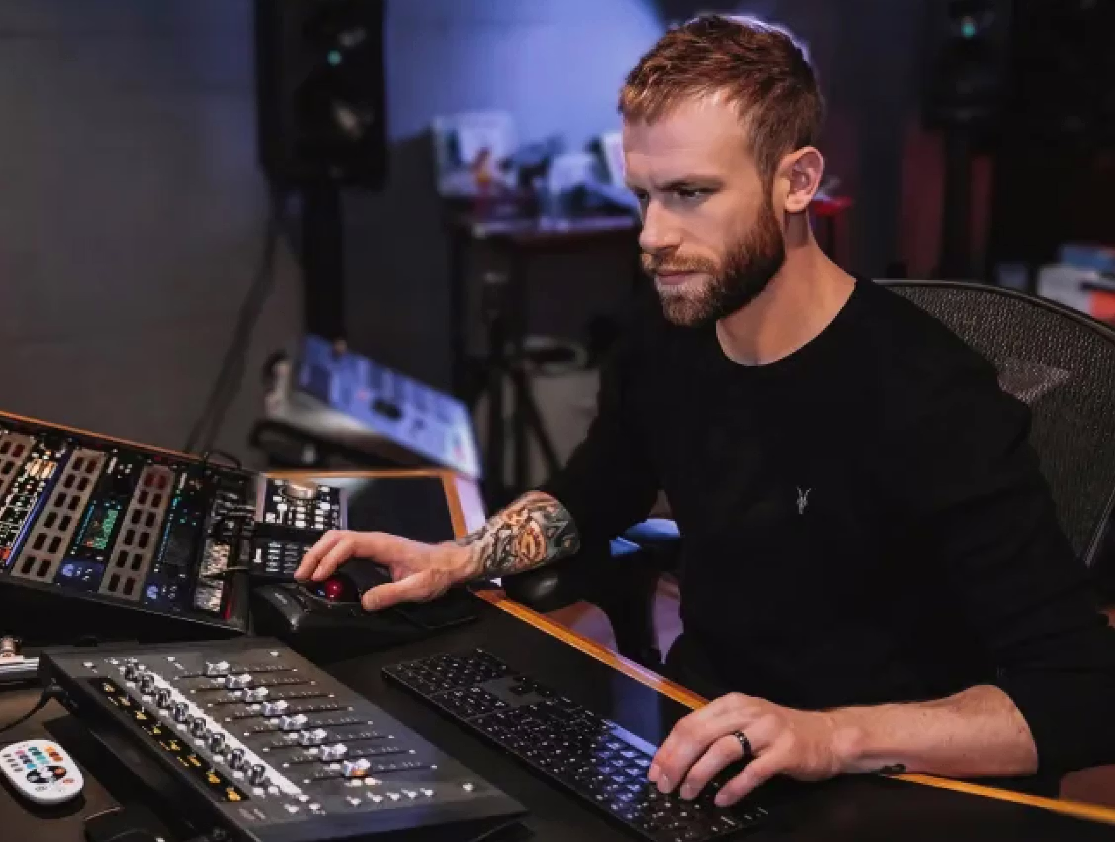 Bearded audio engineer Aaron Mattes working at a professional mixing desk with control surface and analog gear in a modern recording studio.