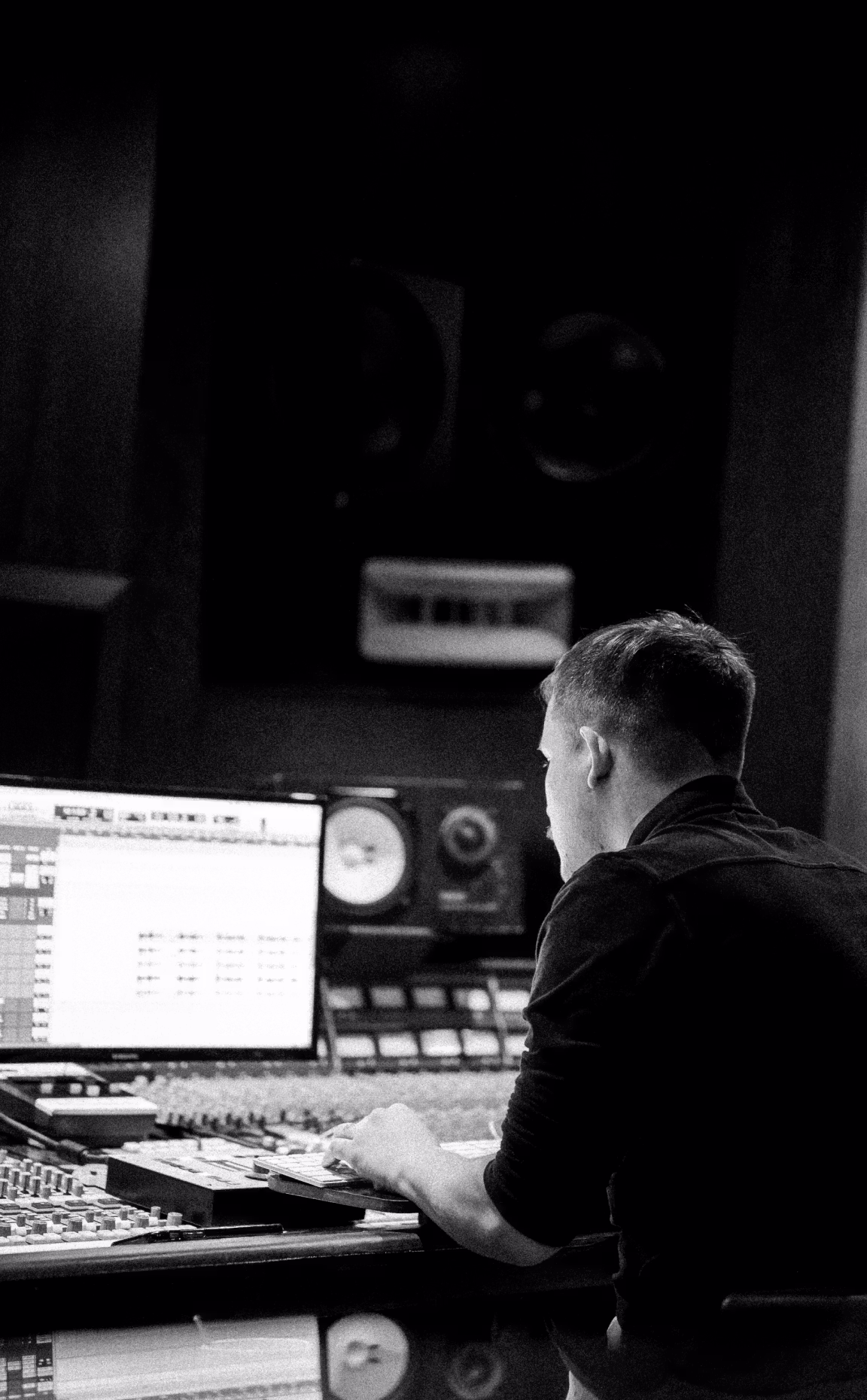 Sound engineer at a mixing console in a professional recording studio, working on a digital audio workstation with large monitor speakers.